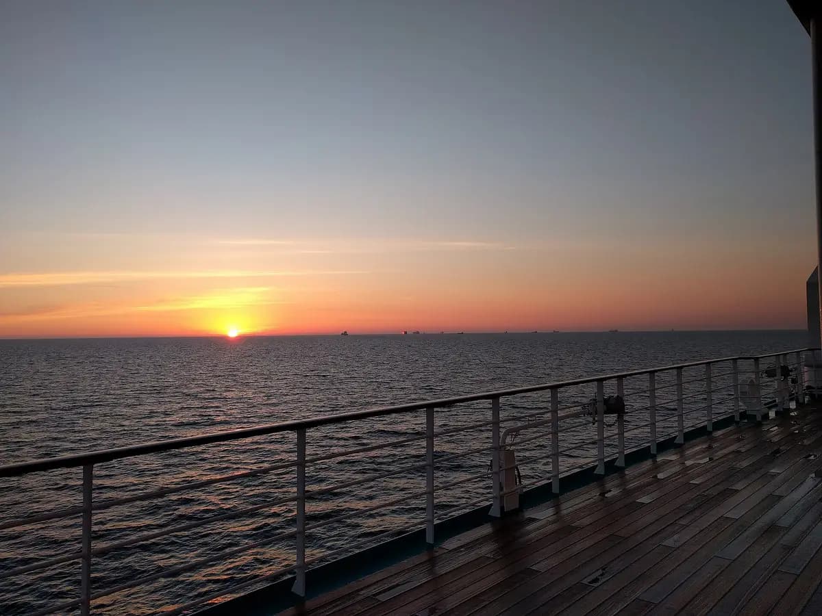 Sunset over open ocean from a cruise ship's rail